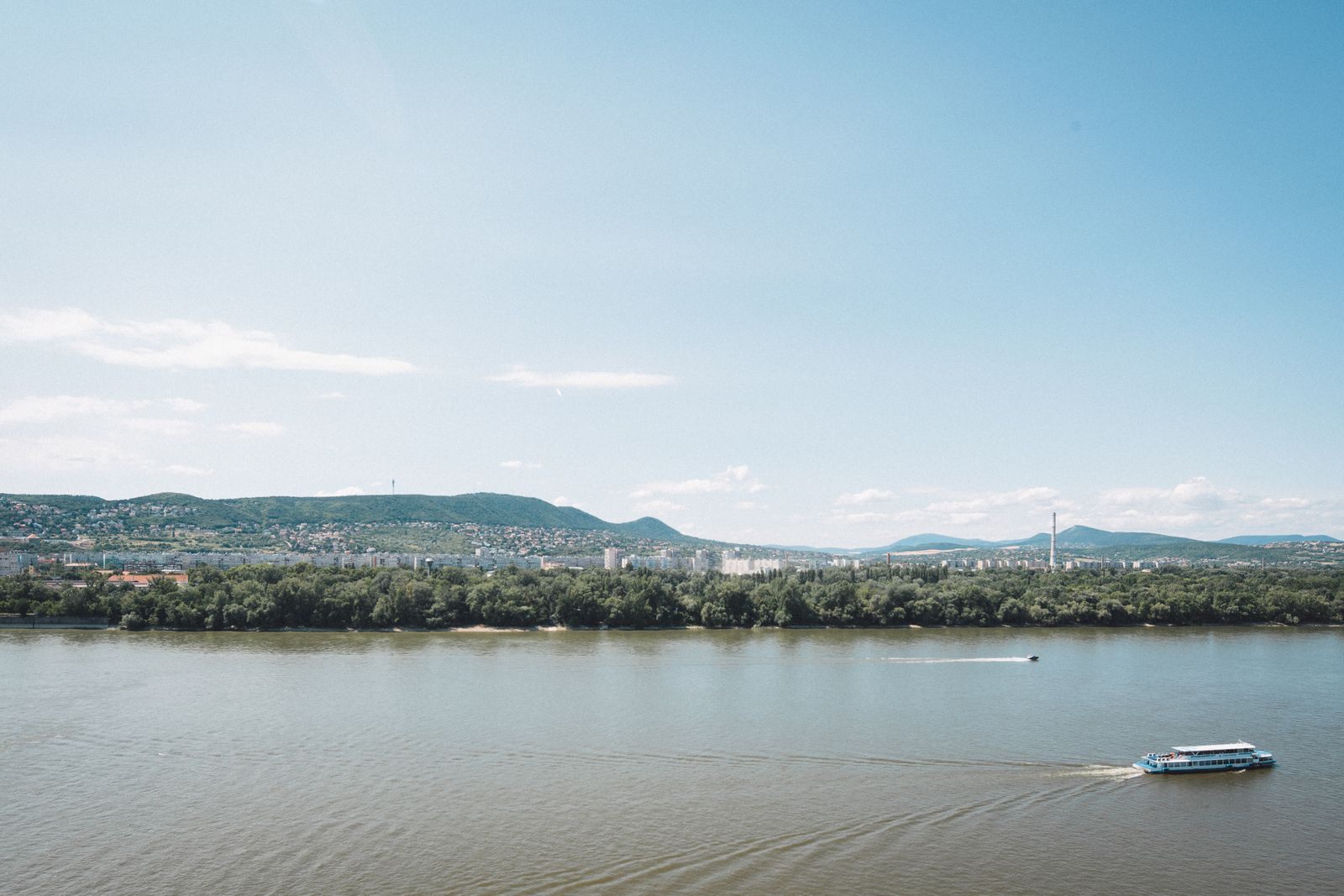A boat on the wide Danube with green hills along the far bank
