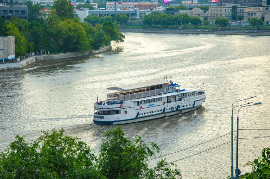 River cruise ship navigating a city waterway lined with trees