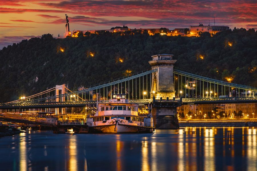 Chain Bridge in Budapest lit at night with boats on the Danube
