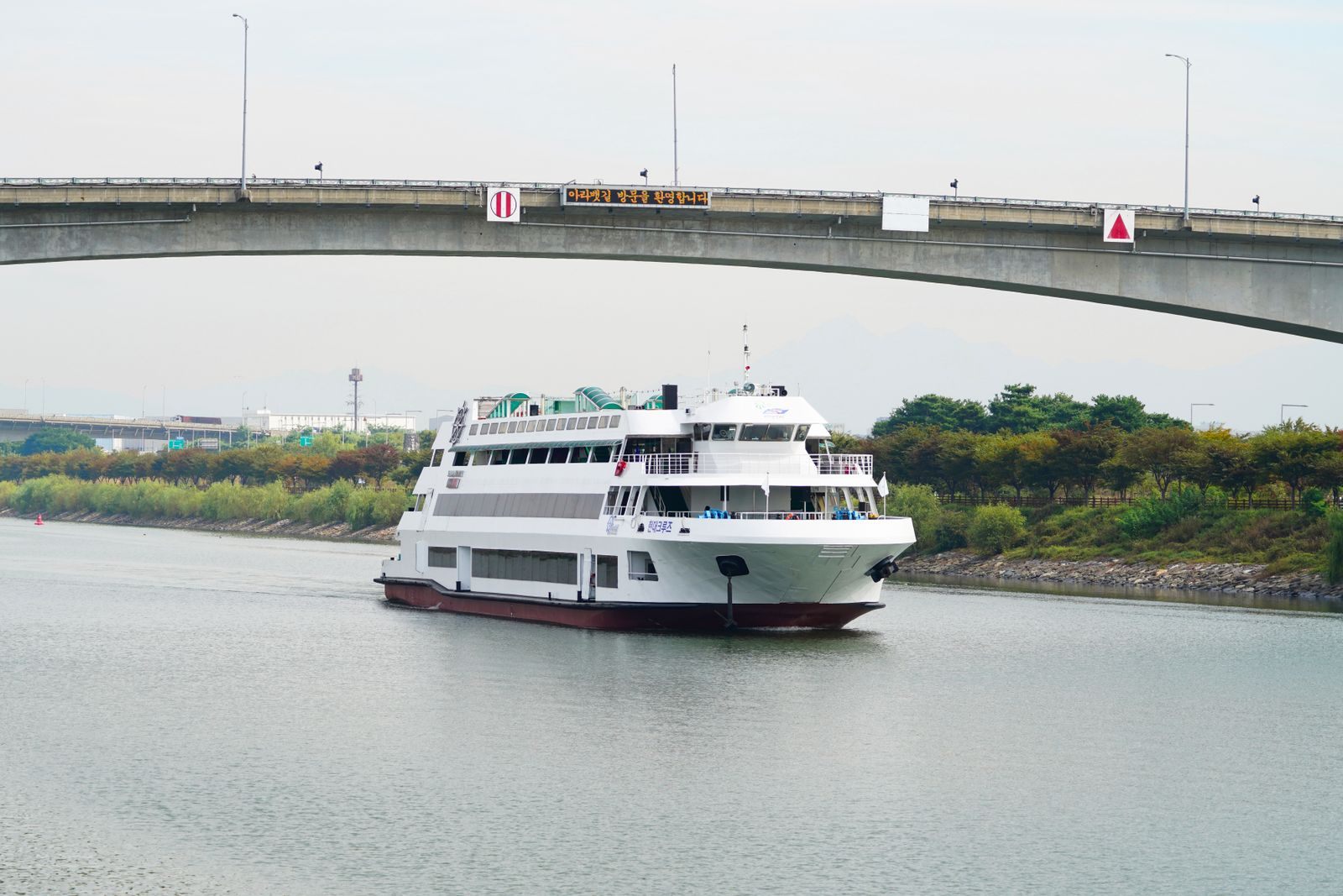 White river cruise ship sailing beneath a bridge on a green, quiet waterway, planning river cruise deals for 2027